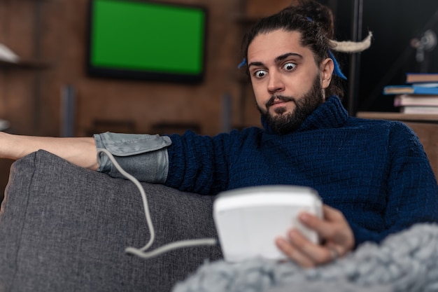 problem with health. unhappy bearded man checking his blood pressure while resting at home