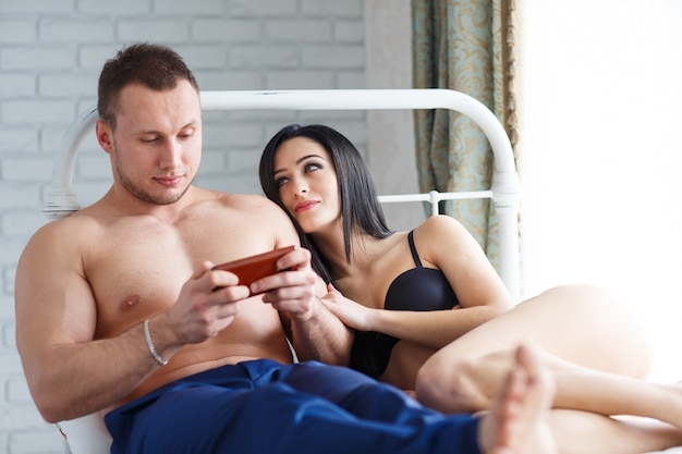 Problems in the family. angry young woman lying on the bed,\
against her husband, who plays the game on the phone.