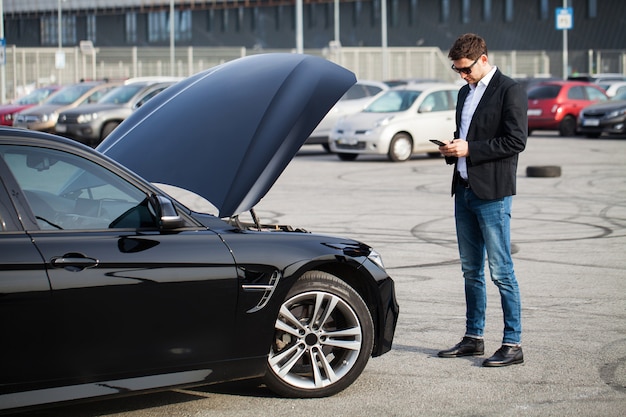 Problems on the road. Man with broken car calling on smartphone