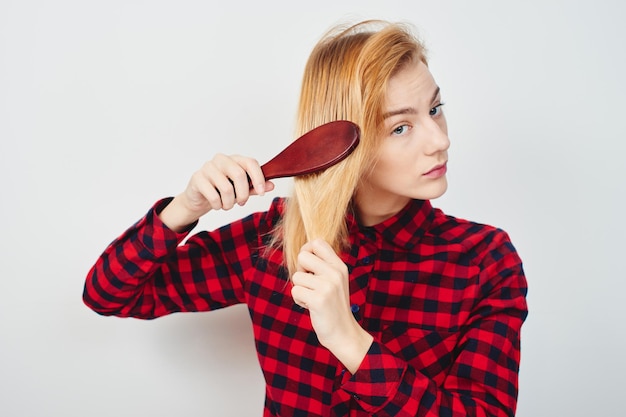 Problems with the hair. Girl with hairbrush on white background in the red shirt