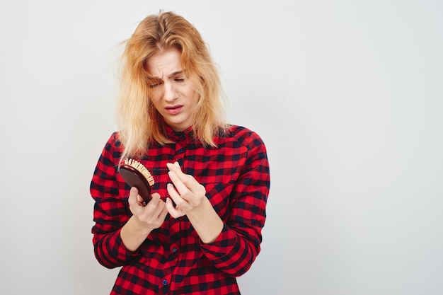 Problems with the hair. Girl with hairbrush on white background in the red shirt