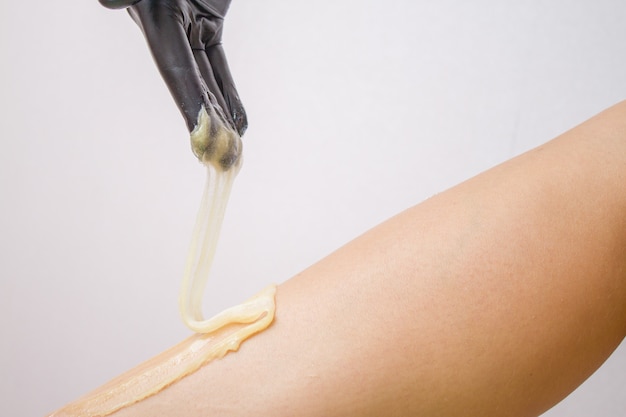 Procedure of hair removing on leg beautiful woman with sugar paste or wax honey and black gloves hand