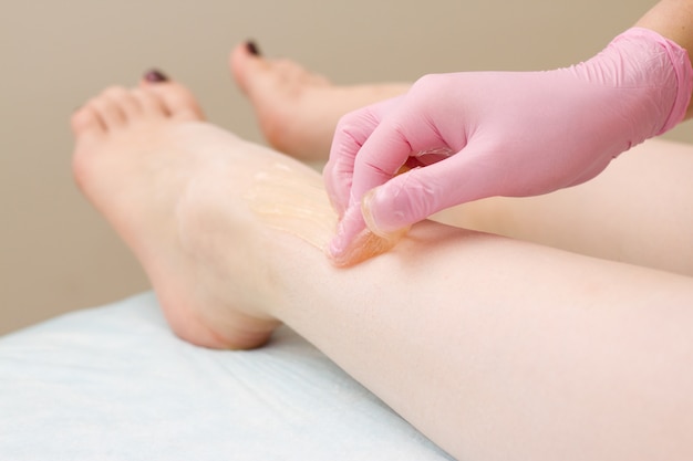 Procedure of hair removing on leg beautiful woman with sugar paste or wax honey and pink gloves hand 