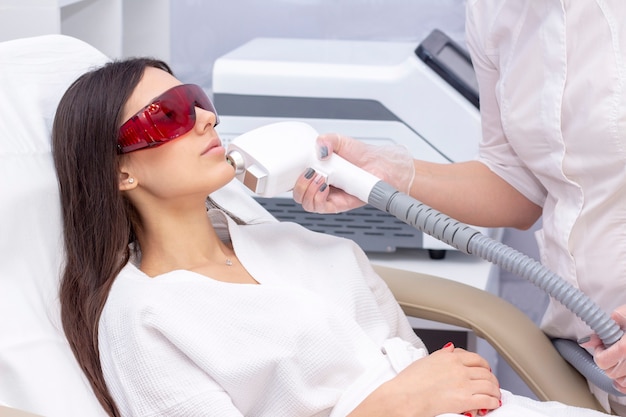 Procedure of photoepilation in the beauty salon. young woman receiving epilation laser treatment on face at beauty center close up