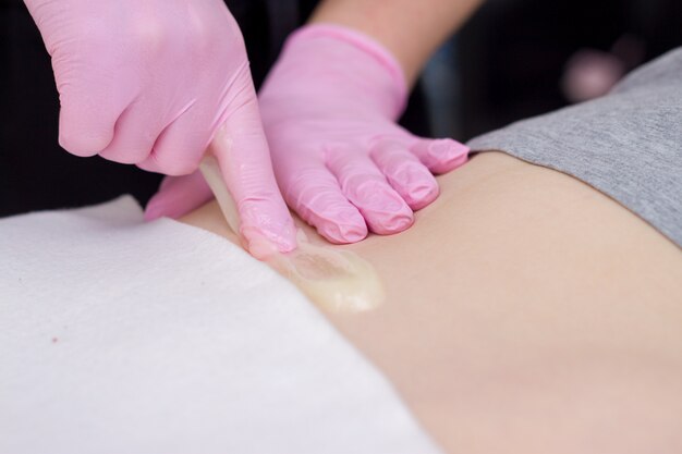 Procedure van haar die op been verwijderen mooie vrouw met suikerdeeg of washoning en roze handschoenenhand