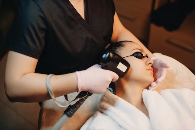 Procedure voor het verwijderen van gezichtshaar gedaan aan een brunette vrouw met behulp van moderne apparaten in de spa salon