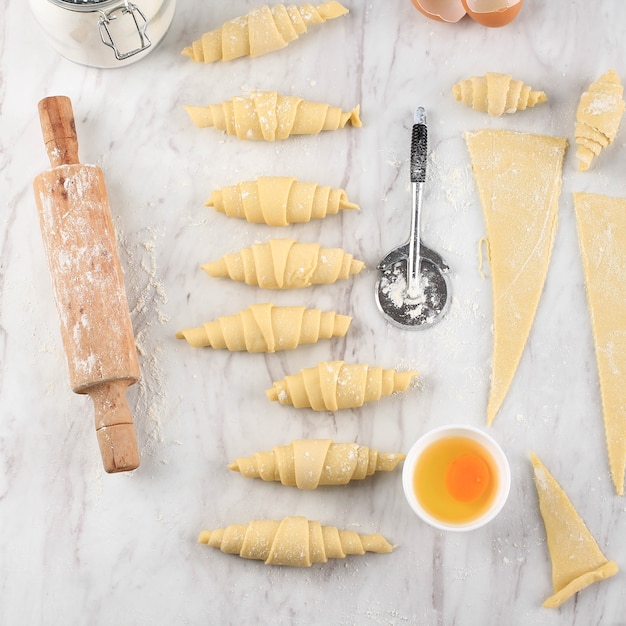 Proces maken van zelfgemaakte Croissant, Raw Croissant Voorbereiding Thuis bakken. Croissant van verschillende grootte boven een witte marmeren tafel