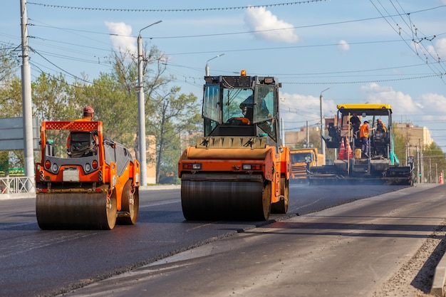 Proces van asfalteermachine en twee walsen tijdens wegenbouwwerkzaamheden aan de nieuwe weg in zomerdag