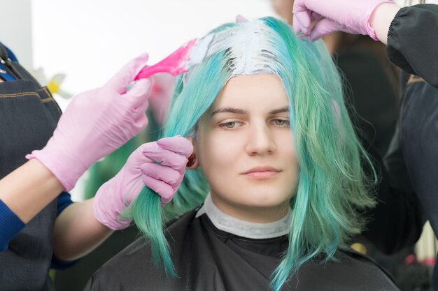 Proces van het bleken van haarwortels in kapsalon. twee kappers in handschoen gebruiken roze borstel terwijl ze verf aanbrengen op jonge volwassen klanten met smaragdgroene haarkleur