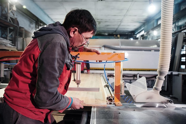 Proces van productie en vervaardiging van houten meubilair in meubelfabriek Arbeider timmerman man in overall verwerkt hout op speciale apparatuur