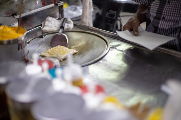 proces voor de bereiding van smakelijke traditionele Thaise pannenkoeken op een straatteller. mannelijke handen bakken een pannenkoek in olie. lokale specialiteit.