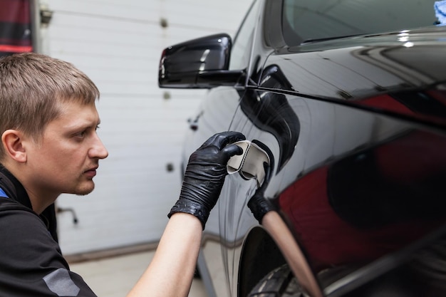 The process of applying a nanoceramic coating on the car's fender by a male worker with a sponge and special chemical composition to protect the paint on the body from scratches chips and damage