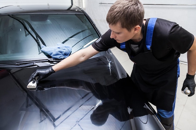 The process of applying a nanoceramic coating on the car's hood by a male worker with a sponge and special chemical composition to protect the paint on the body from scratches chips and damage