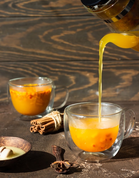 Process brewing tea, hot colorful sea buckthorn tea is poured into a glass cup