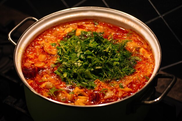 the process of cooking borsch in a saucepan on the dark background. national cuisine