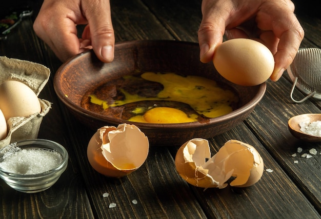 料理のテーブルの上で卵を調理するプロセス 健康的な卵のダイエット 料理人は料理テーブル上の皿の上で卵を壊そうとしています