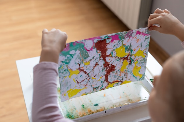 Process of creating drawing Ebru. Child draws with paints on water
