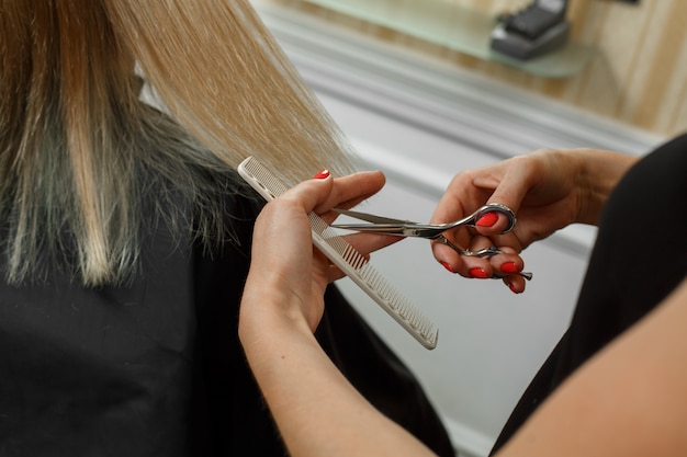 process of haircuts. hairdresser with scissors and comb in the hands.  hairdresser will cut the ends of the well groomed blonde hair. courses for hairdressers.