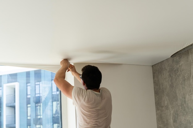 Process of installing stretch ceiling in the hall. Close up of the hand of man with a tool.