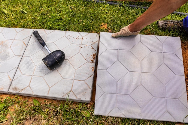 The process of laying tiles on the garden path by a\
professional worker in white construction gloves country\
construction garden design