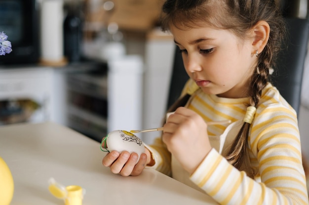 Process of little girl painting eggs on kitchen spring holiday easter decoration at home side view