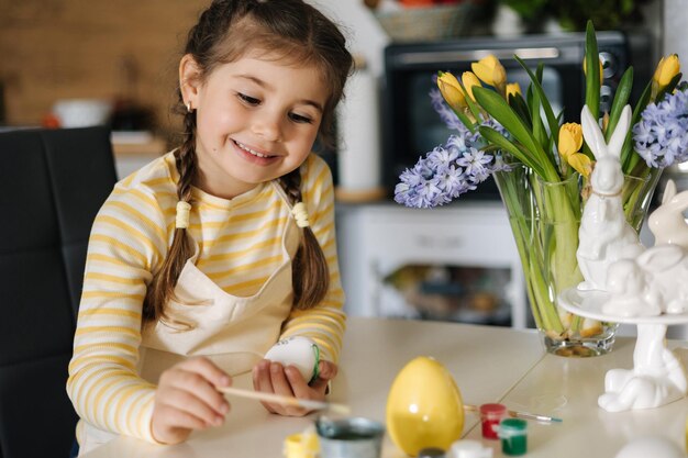 Process of little girl painting eggs on kitchen spring holiday easter decoration at home side view