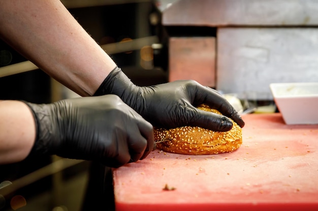 The process of making a burger in a restaurant kitchen The chef in black gloves cut the bun