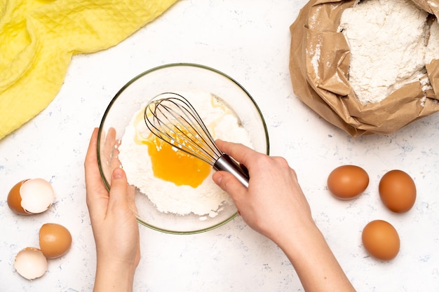 The process of making dough for pancakes with ingredients on a light table, eggs and flour are whipped with a mixer