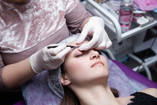 Process of making eyebrows. Pretty woman with closed eyes on the procedure.