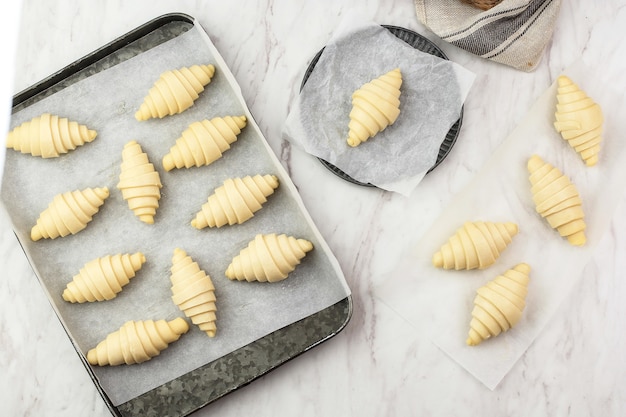 Processo di preparazione del croissant fatto in casa, preparazione del croissant crudo al forno a casa. croissant di varie dimensioni sopra il tavolo in marmo bianco