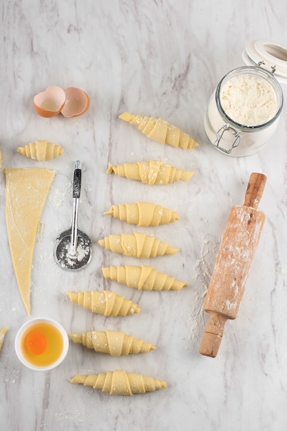 Foto processo di preparazione del croissant fatto in casa, preparazione del croissant crudo al forno a casa. croissant di varie dimensioni sopra il tavolo in marmo bianco