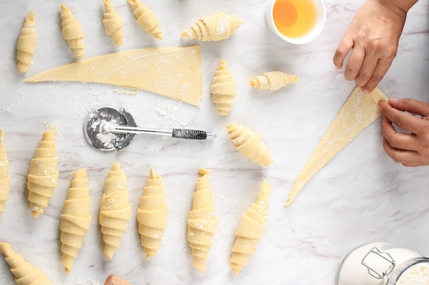 Foto processo di preparazione del croissant fatto in casa, preparazione del croissant crudo al forno a casa. croissant di varie dimensioni sopra il tavolo in marmo bianco