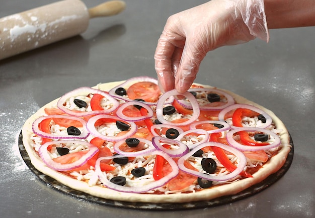 The process of making pizza the dough with a nocturnal lies on the table A woman's hand adds an onion to the pizza Behind lies a rock