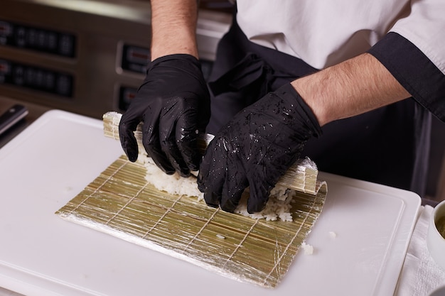 Process of making sushi and rolls at restaurant kitchen. Chefs hands with knife.