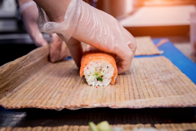 Process of making sushi and rolls at restaurant kitchen. Chefs hands with knife.