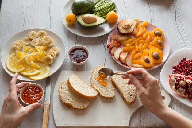 Processo di preparazione di toast dolci con marmellata e vari frutti albicocche, pesche, banane, arance e avocado decorate con melograni in cima.