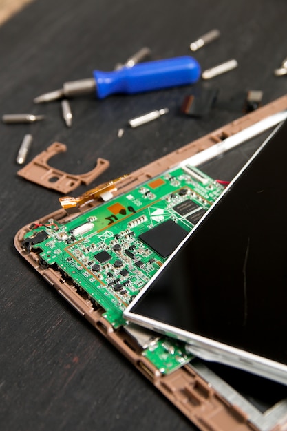 Process of PC Tablet device repair near screwdriver and bit on black wooden background. 