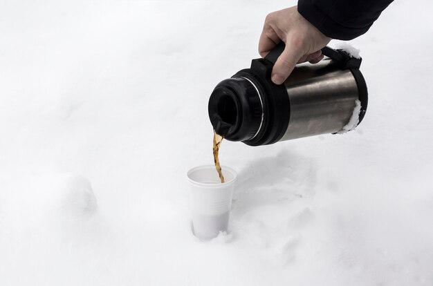 自然の雪の吹きだまりの中で冬に使い捨てのグラスにコーヒーを注ぐプロセス。