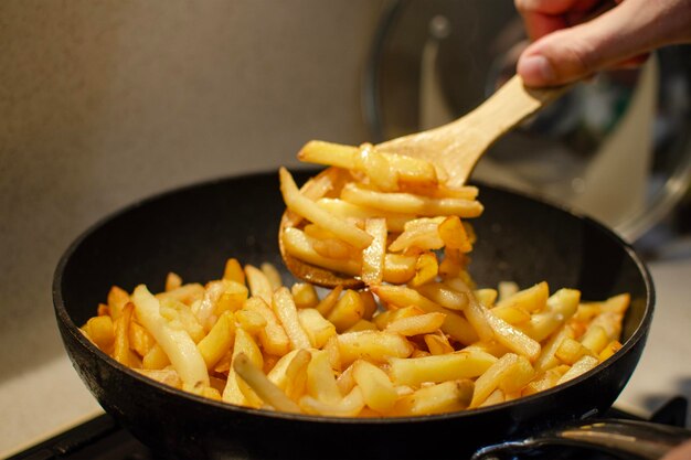 Foto il processo di preparazione delle patate fritte preparazione di un contorno per la carne una mano trasforma le patate fritte