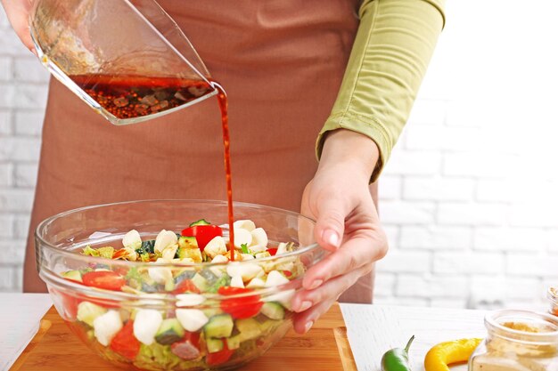 Foto processo di preparazione della salsa per l'insalata in cucina donna che versa la salsa in una ciotola di vetro con ingredienti per l'insalata