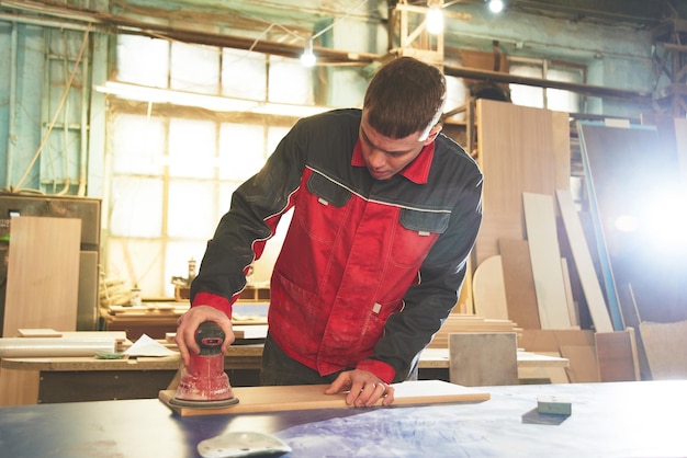 Process of production and manufacture of wooden furniture in
furniture factory worker carpenter man in overalls processes wood
on special equipment