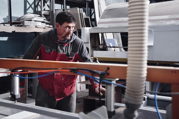 家具工場での木製家具の製造と製造のプロセスオーバーオールの労働者大工の男は、特別な機器で木材を処理します