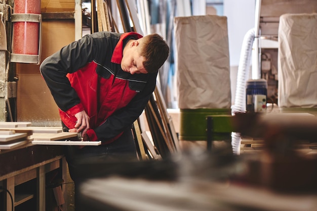 Process of production and manufacture of wooden furniture in
furniture factory worker carpenter man in overalls processes wood
on special equipment