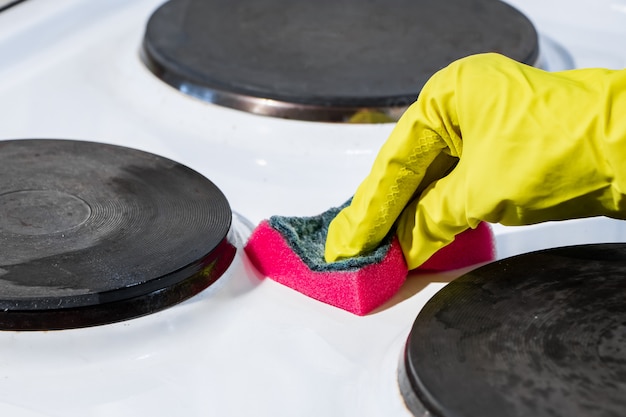 The process of washing an electric stove. A hand in a yellow glove cleans the white surface of dirt. 