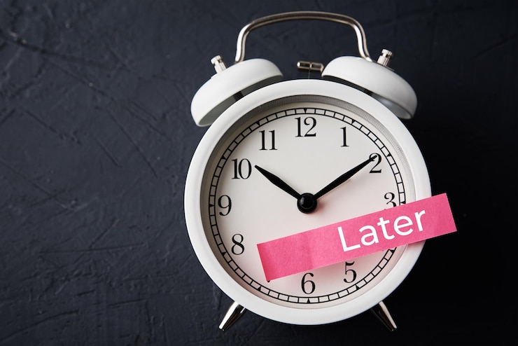 Photo procrastination and delay concept sticky note with word later on the white alarm clock