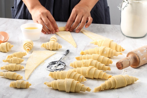 Producing classic croissants at the bakery shop Woman is rolling dough into rolls for further baking French pastry goods