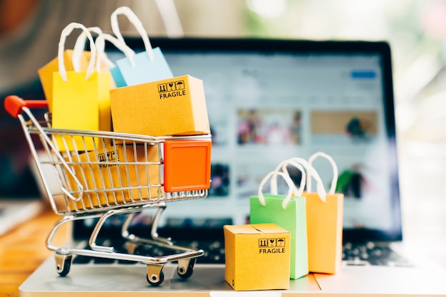 Contenitori di prodotti del prodotto e shopping bag nel carrello con il computer portatile per lo shopping online e il concetto di consegna