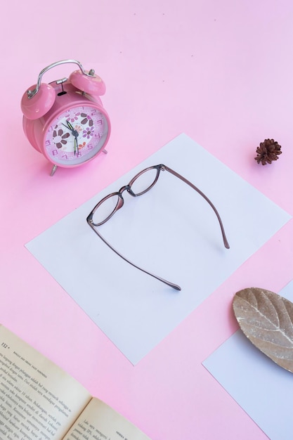 Product Presentation of Minimalist Concept Idea eyeglasses book clock dry leaves on pink paper background