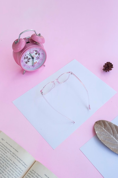 핑크색 종이 배경에 미니멀리즘 개념 아이디어 안경 책 시계 마른 잎의 제품 프레젠테이션