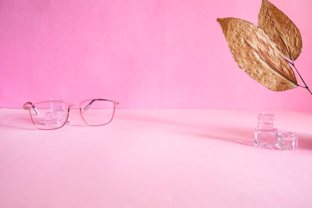 Foto idea di concetto minimalista di presentazione del prodotto. bicchieri, foglie secche, cubetti di ghiaccio su sfondo di carta rosa.